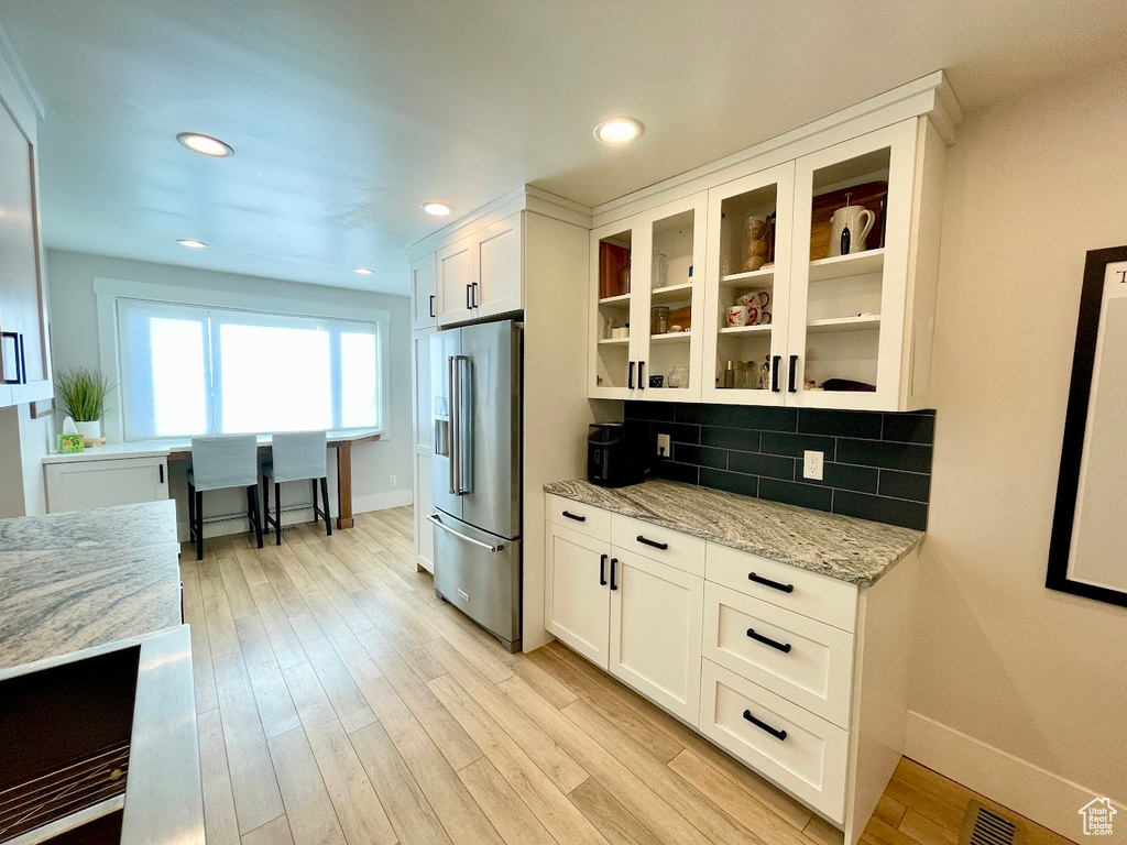 Kitchen featuring white cabinets, light stone countertops, high quality fridge, and light hardwood / wood-style floors