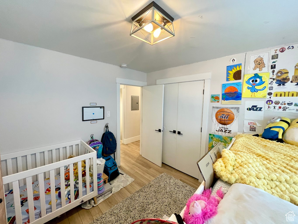 Bedroom featuring electric panel, a crib, a closet, and light wood-type flooring