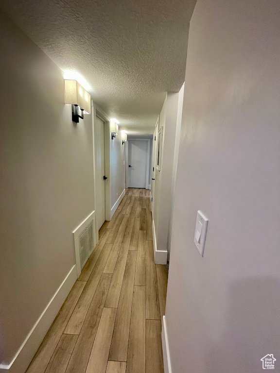 Hall with a textured ceiling and light hardwood / wood-style floors