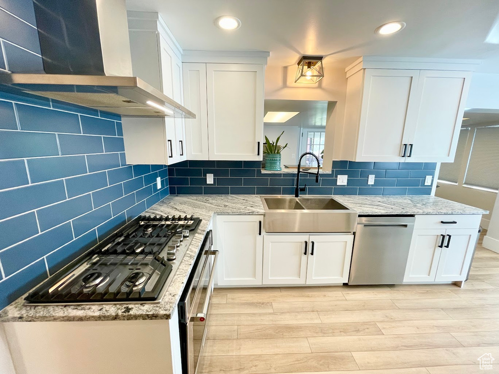 Kitchen with white cabinetry, stainless steel appliances, wall chimney exhaust hood, and sink