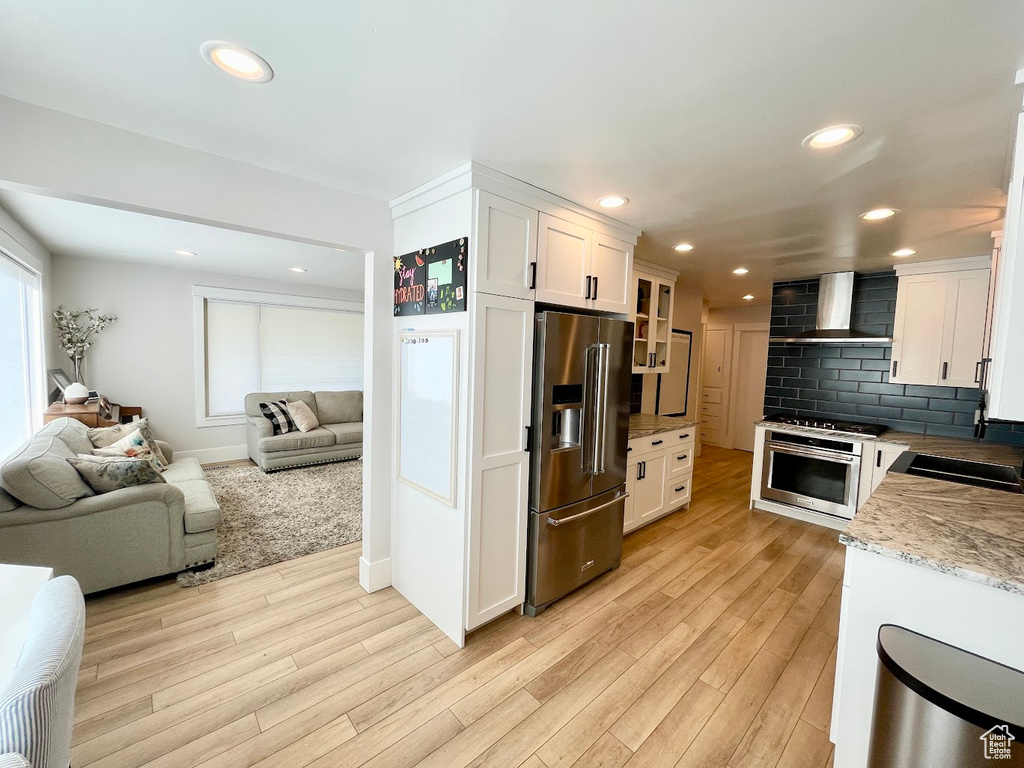 Kitchen with stainless steel appliances, wall chimney range hood, white cabinets, and light wood-type flooring