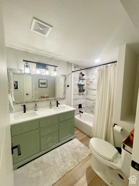 Full bathroom featuring a textured ceiling, hardwood / wood-style floors, shower / bath combo with shower curtain, vanity, and toilet