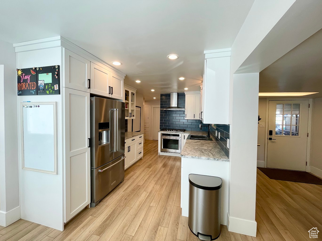 Kitchen with stainless steel appliances, light hardwood / wood-style floors, wall chimney exhaust hood, and white cabinetry