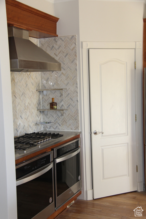 Kitchen featuring hardwood / wood-style flooring, tasteful backsplash, wall chimney exhaust hood, and stainless steel appliances