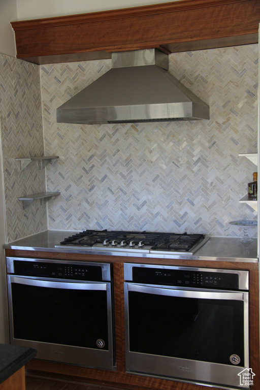 Kitchen with stainless steel appliances, wall chimney exhaust hood, and tasteful backsplash