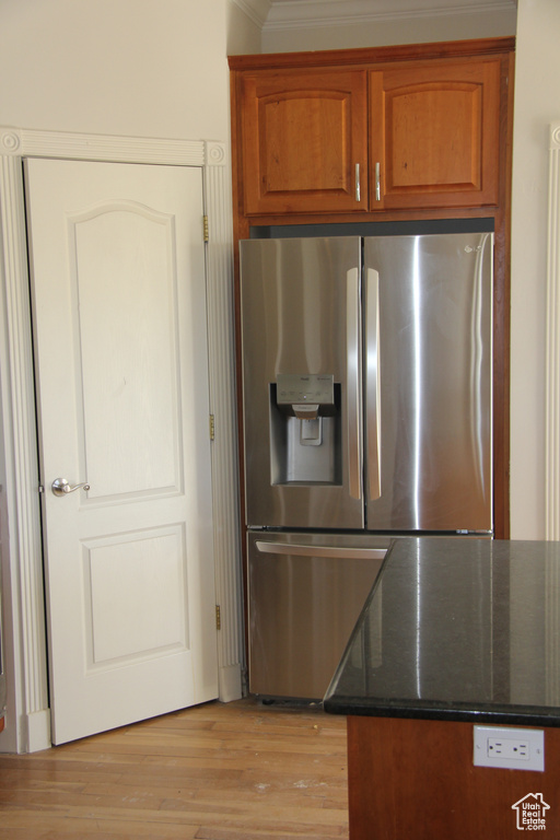 Kitchen featuring stainless steel refrigerator with ice dispenser, dark stone countertops, light wood-type flooring, and crown molding