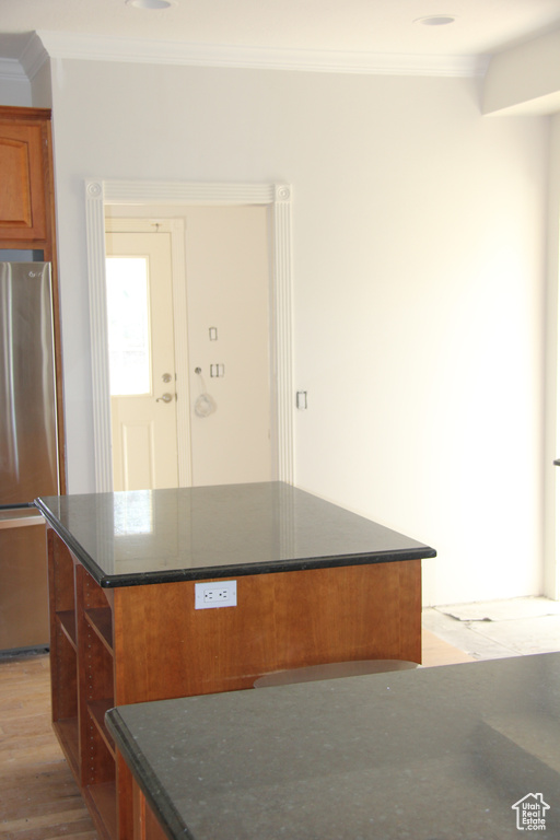 Kitchen featuring ornamental molding, stainless steel fridge, dark stone counters, light hardwood / wood-style floors, and a center island