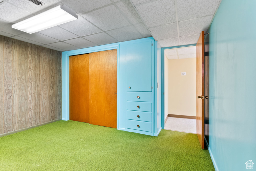 Unfurnished bedroom with wood walls, a paneled ceiling, carpet, and a closet