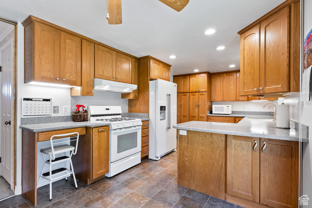 Kitchen with kitchen peninsula, white appliances, sink, and a kitchen bar