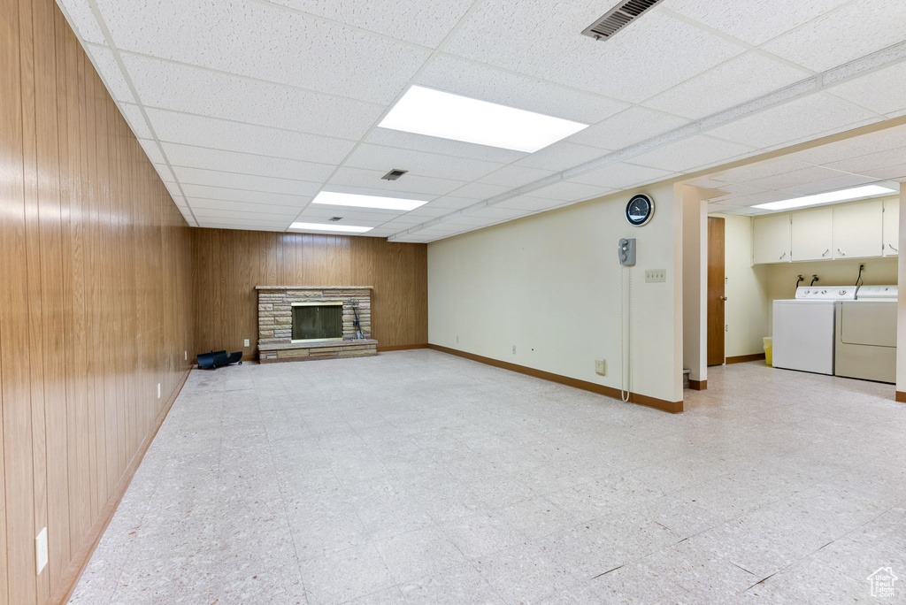 Unfurnished living room featuring a drop ceiling, wooden walls, separate washer and dryer, and a fireplace