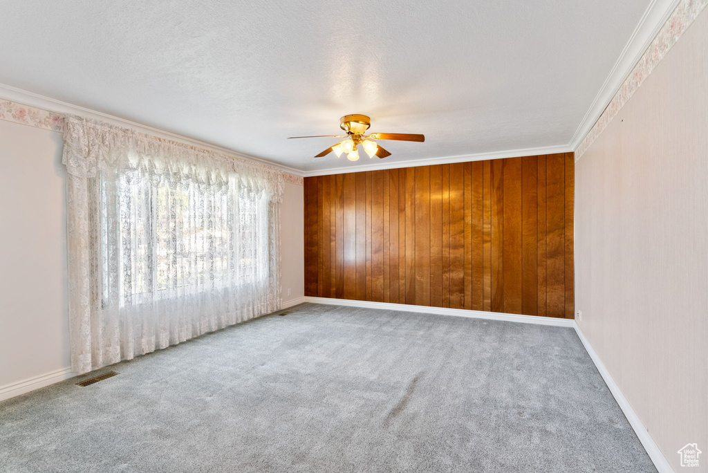 Carpeted spare room with ornamental molding, a textured ceiling, wood walls, and ceiling fan