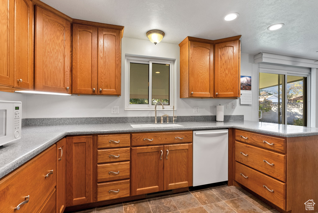 Kitchen featuring white appliances, a textured ceiling, sink, and kitchen peninsula