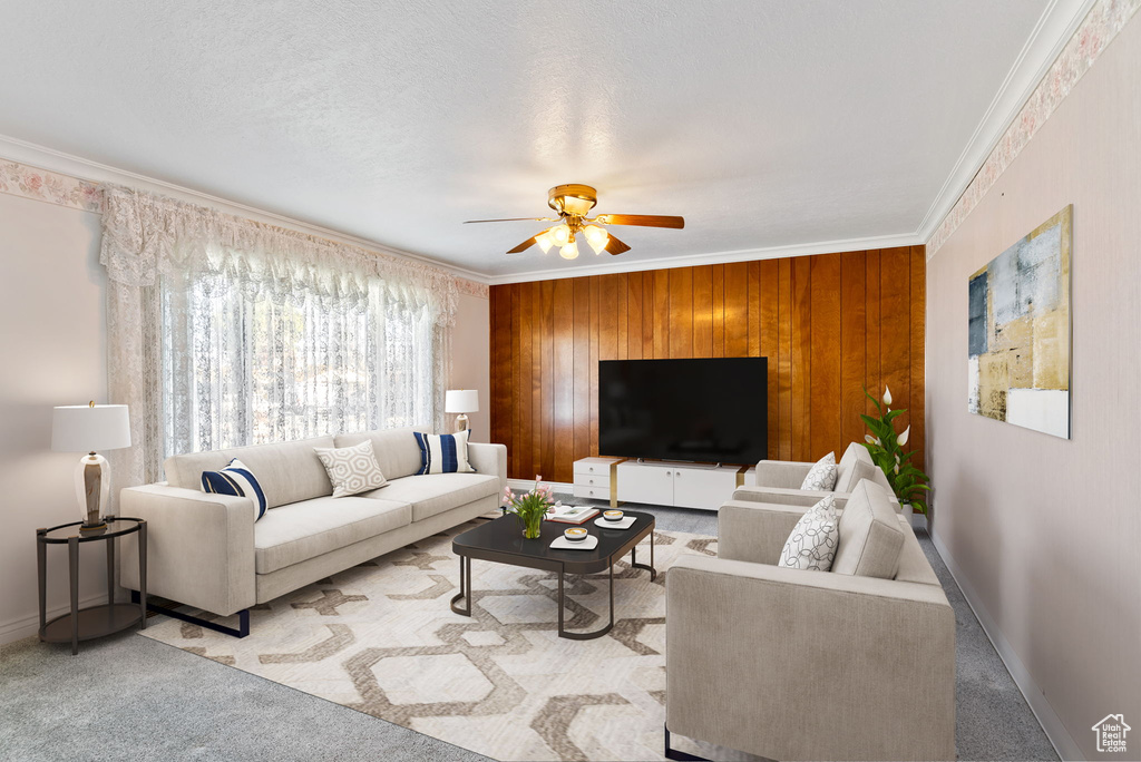 Living room with ornamental molding, a textured ceiling, wooden walls, light colored carpet, and ceiling fan