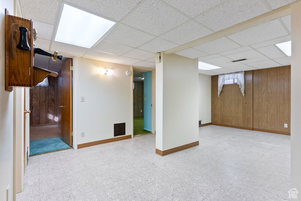 Basement featuring wooden walls and a drop ceiling