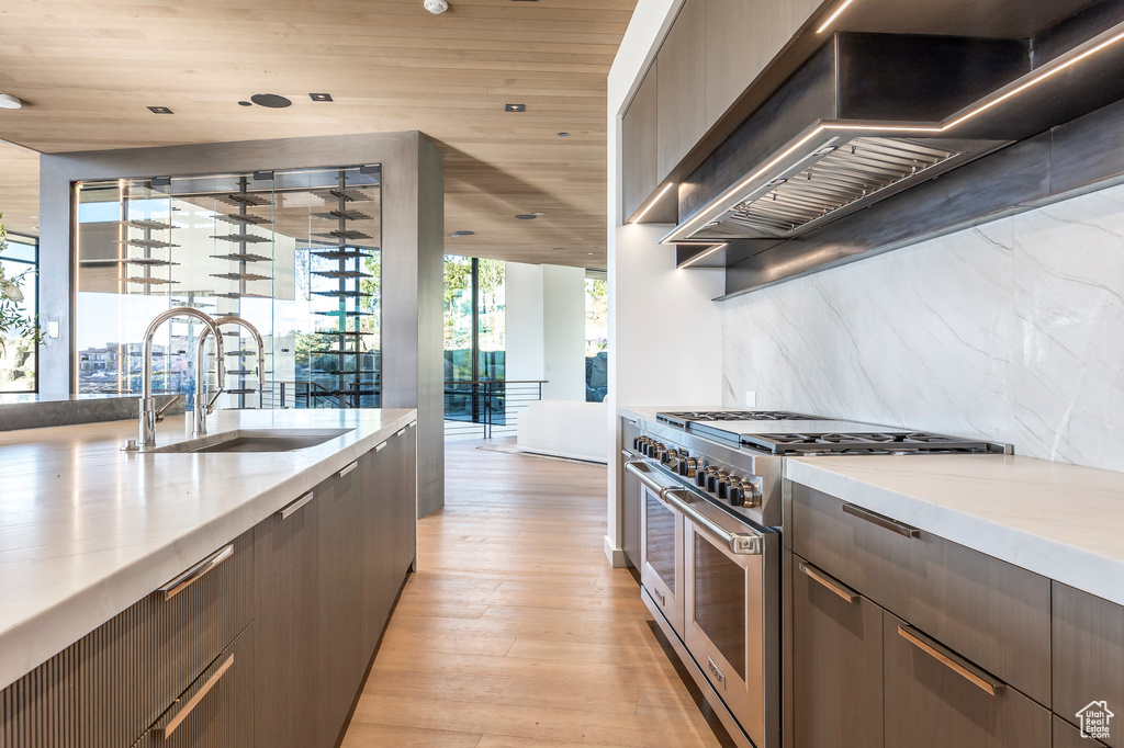 Kitchen with double oven range, wall chimney range hood, a sink, light wood finished floors, and wood ceiling