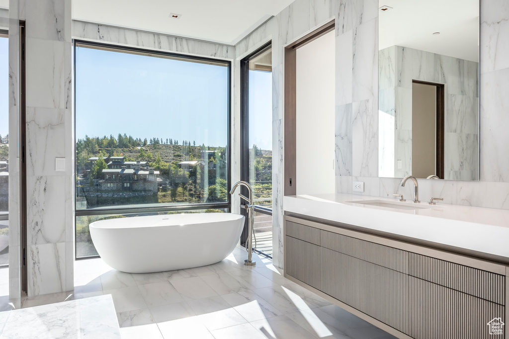 Full bathroom featuring a soaking tub, vanity, and marble tiled floors