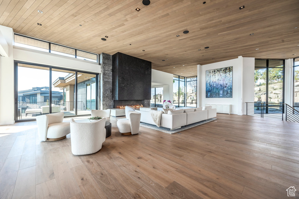 Living area with wood ceiling, floor to ceiling windows, wood-type flooring, and a large fireplace