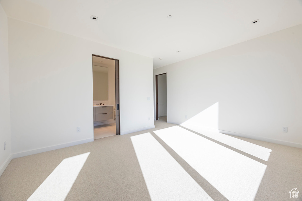 Unfurnished bedroom featuring light carpet, baseboards, and ensuite bathroom