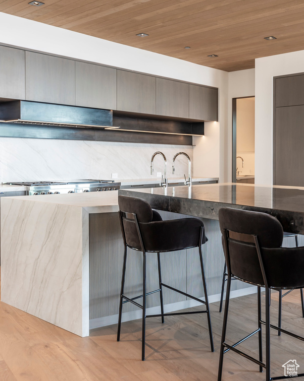 Kitchen featuring a breakfast bar, backsplash, dark stone countertops, wooden ceiling, and modern cabinets