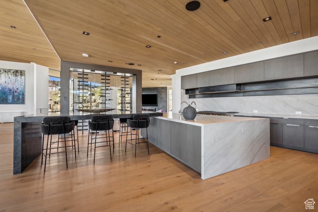 Kitchen with modern cabinets, wood ceiling, gray cabinetry, light wood finished floors, and a breakfast bar