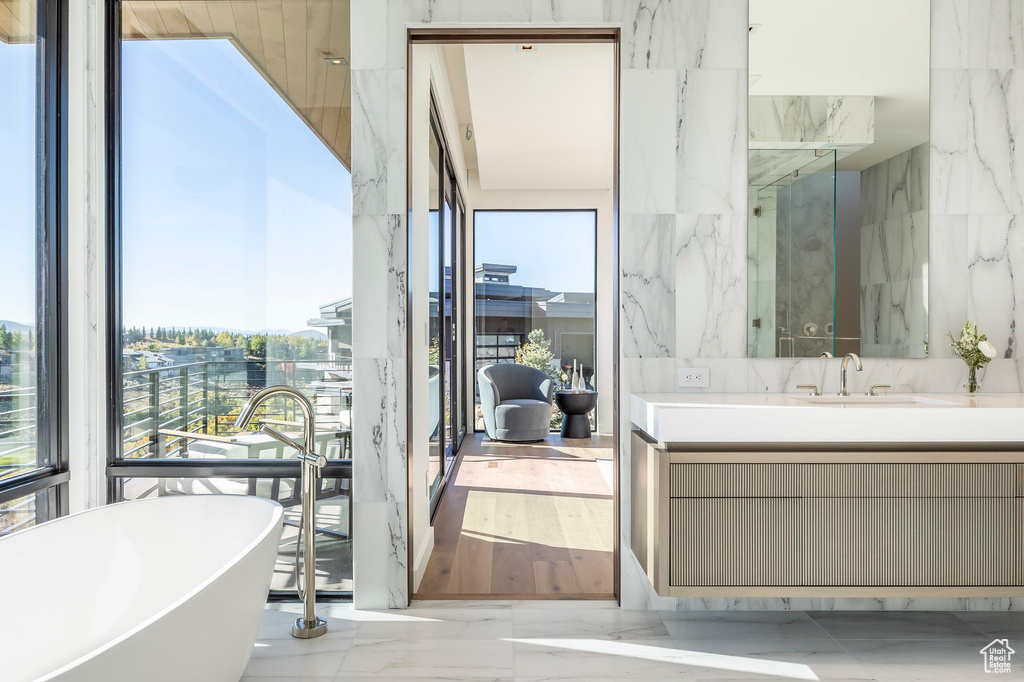 Bathroom featuring marble tiled floors, healthy amount of natural light, a soaking tub, and vanity