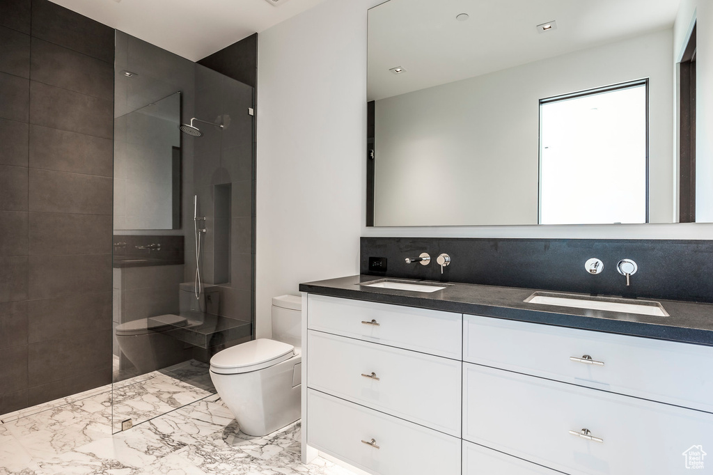 Bathroom featuring toilet, marble finish flooring, a walk in shower, and double vanity