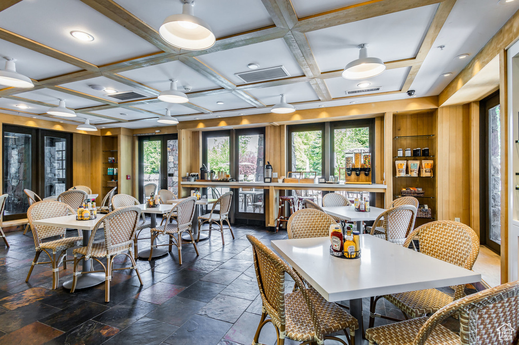 Dining area featuring coffered ceiling, a ceiling fan, stone tile flooring, and beam ceiling