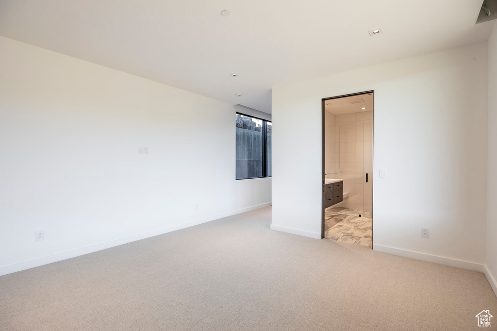 Unfurnished bedroom with light colored carpet, baseboards, and ensuite bath