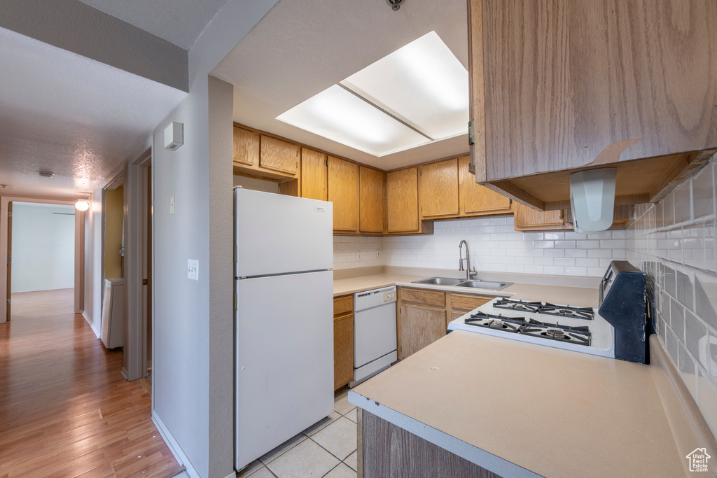 Kitchen with white appliances, sink, light hardwood / wood-style flooring, and decorative backsplash