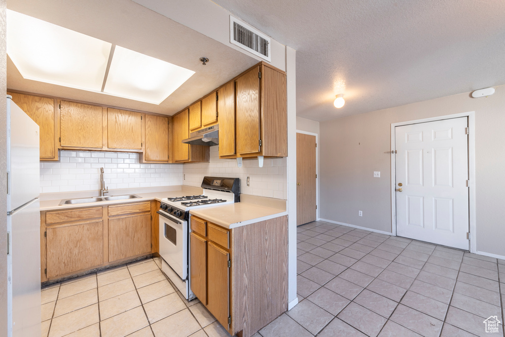 Kitchen featuring decorative backsplash, sink, white appliances, and light tile patterned floors