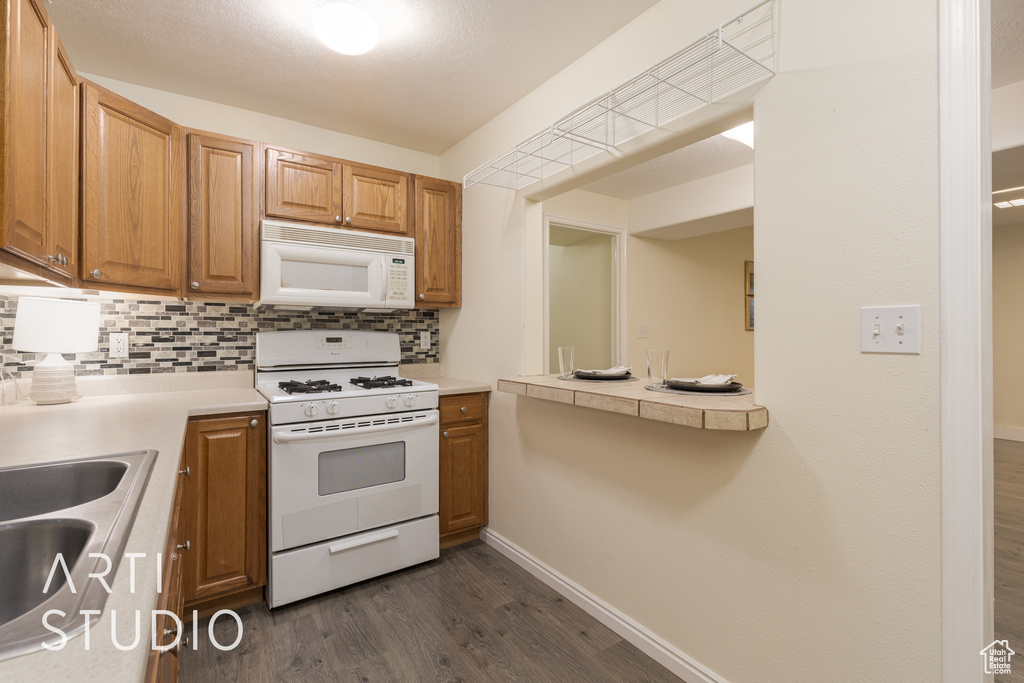 Kitchen featuring white appliances, dark hardwood / wood-style floors, sink, and backsplash