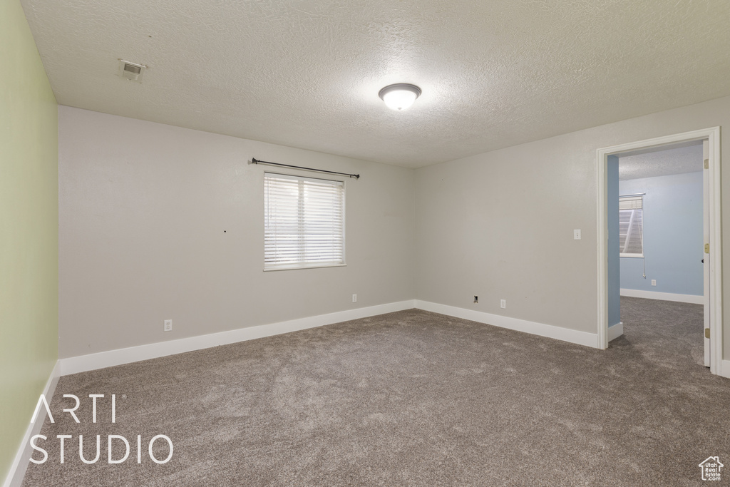 Unfurnished room with a textured ceiling and dark colored carpet