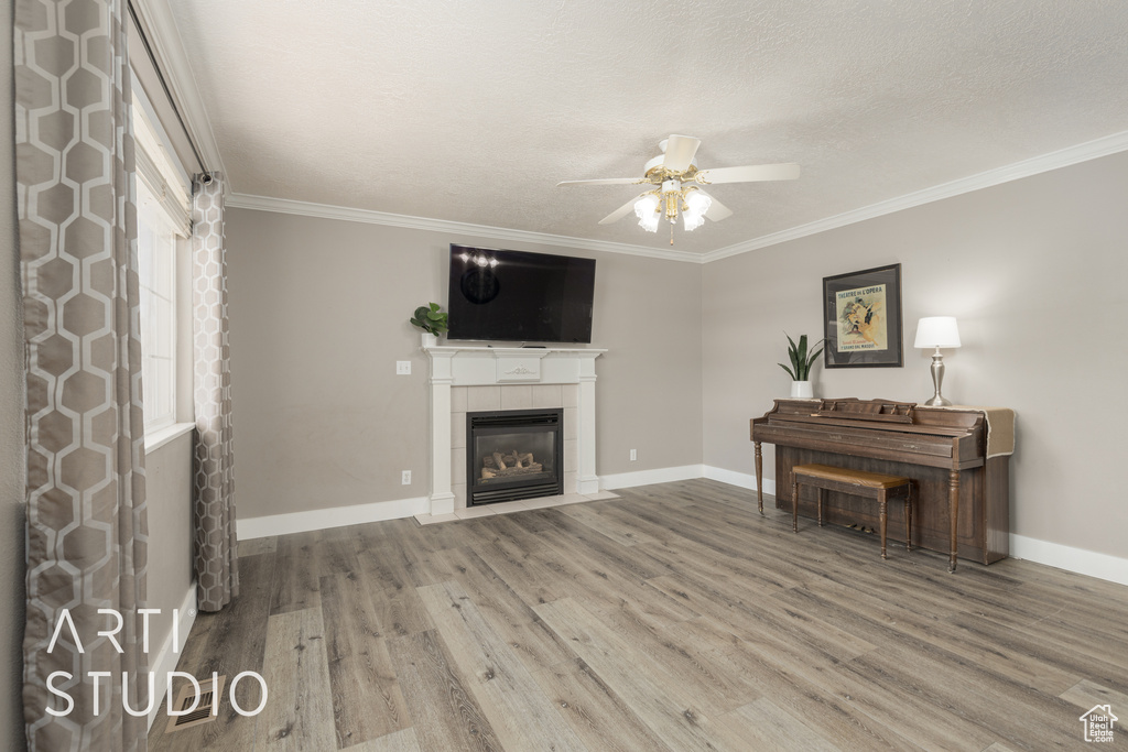 Living room featuring ornamental molding, hardwood / wood-style floors, a tiled fireplace, and ceiling fan