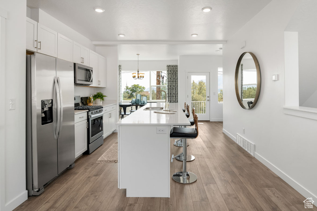 Kitchen with white cabinets, an island with sink, light hardwood / wood-style floors, and stainless steel appliances