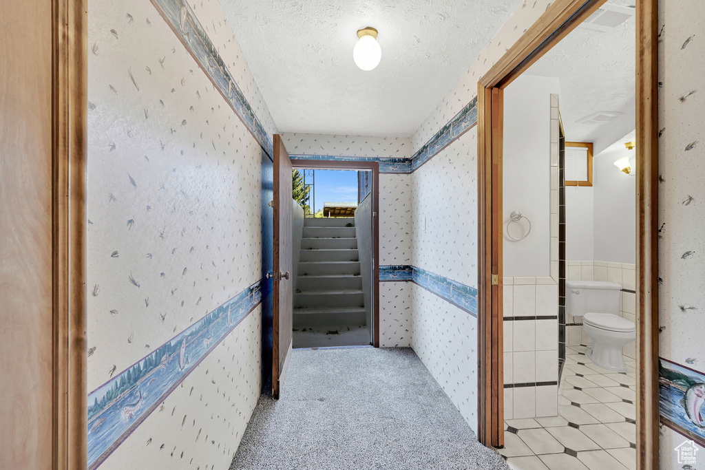 Hallway featuring light colored carpet, a textured ceiling, and tile walls