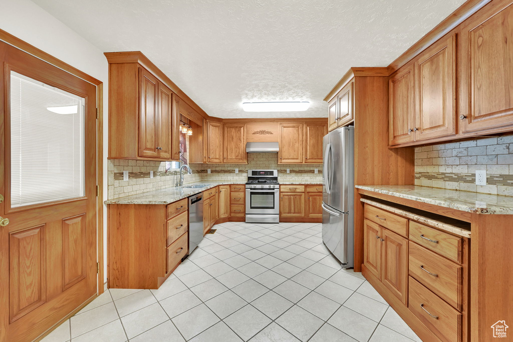 Kitchen with stainless steel appliances, sink, backsplash, and light stone counters