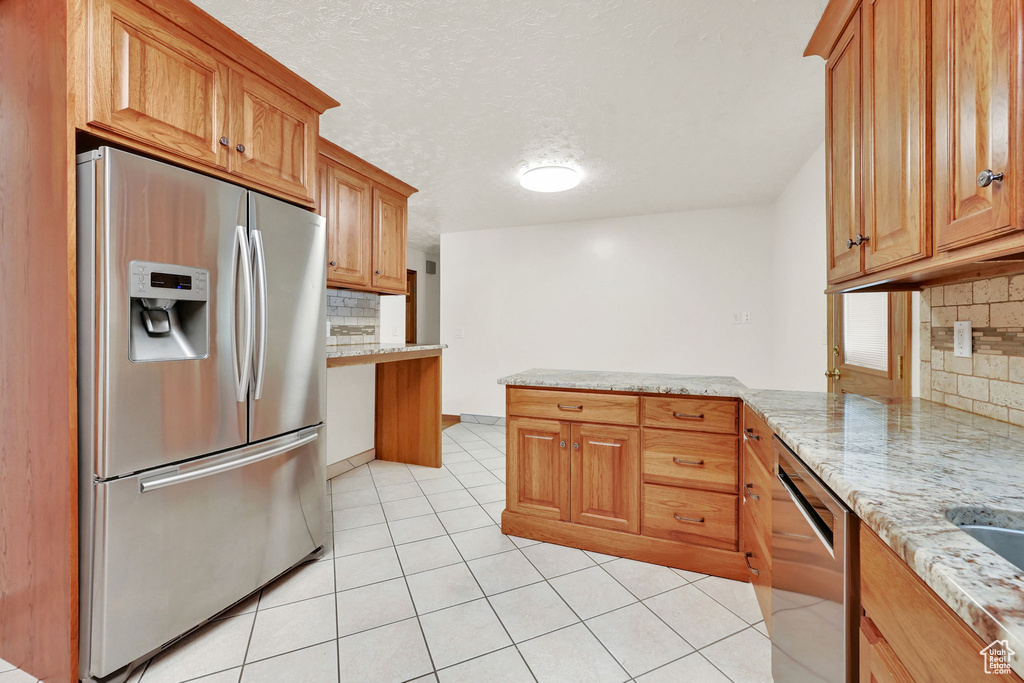 Kitchen with kitchen peninsula, stainless steel appliances, backsplash, and light stone countertops