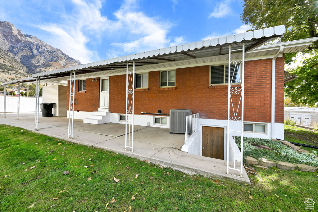 Rear view of property featuring central AC unit, a patio area, a lawn, and a mountain view