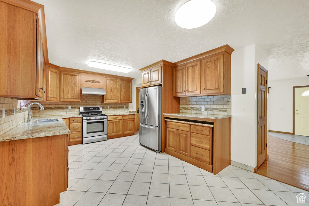 Kitchen featuring a textured ceiling, appliances with stainless steel finishes, sink, and range hood