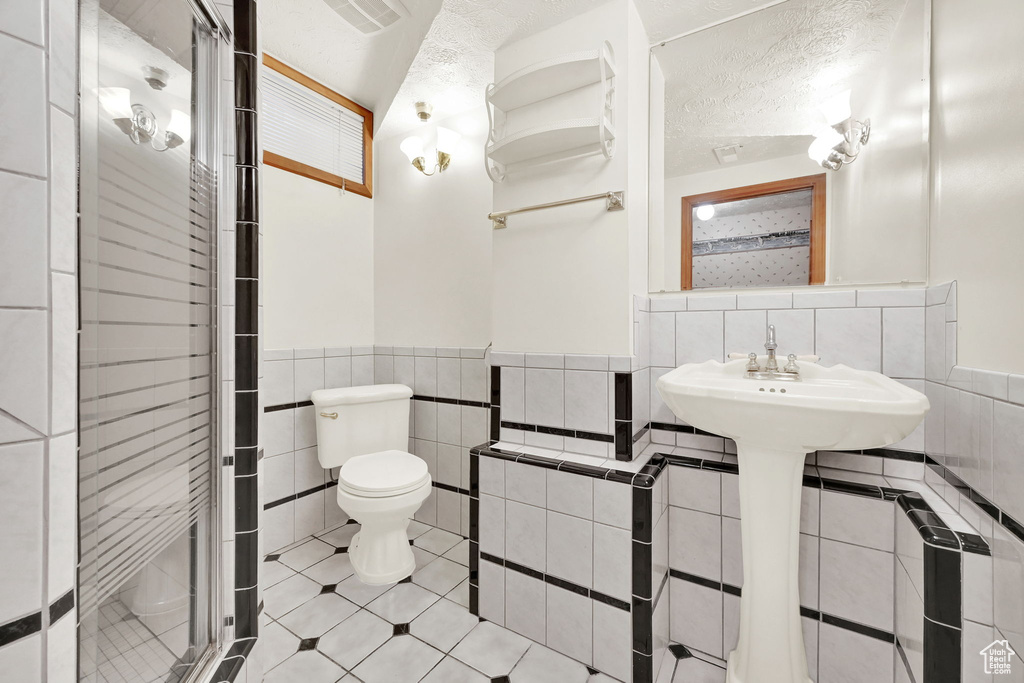 Bathroom featuring a shower with shower door, a textured ceiling, toilet, and tile walls