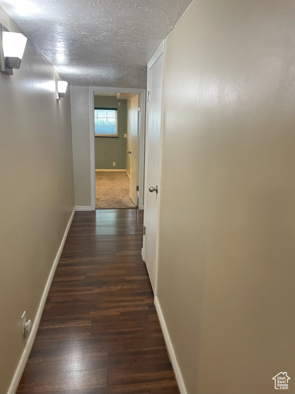 Corridor with dark wood-style floors, baseboards, and a textured ceiling