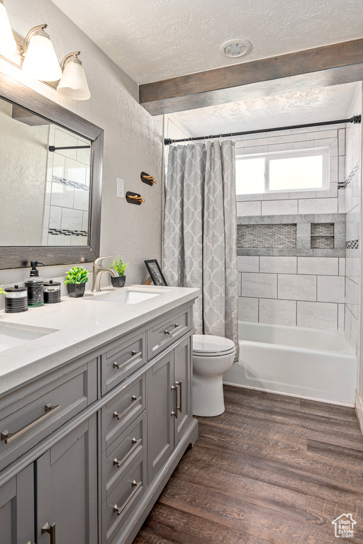 Full bathroom with wood-type flooring, shower / bath combo with shower curtain, toilet, a textured ceiling, and vanity