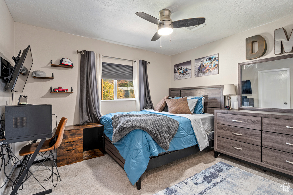 Carpeted bedroom with ceiling fan and a textured ceiling