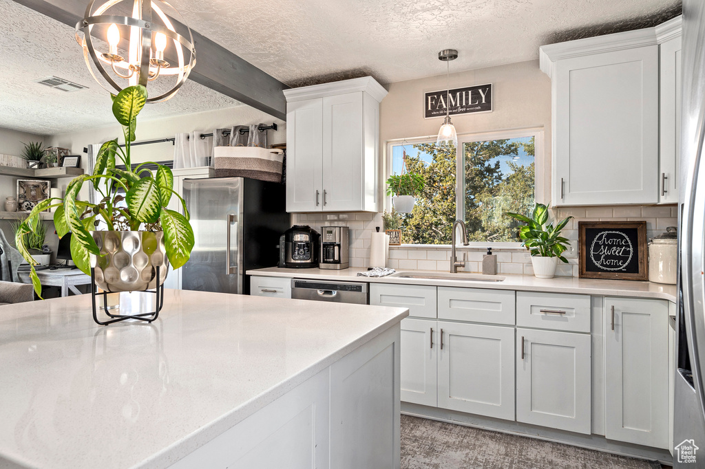 Kitchen featuring backsplash, appliances with stainless steel finishes, pendant lighting, sink, and white cabinets