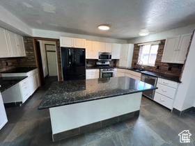 Kitchen featuring white cabinetry, sink, appliances with stainless steel finishes, dark stone countertops, and a kitchen island