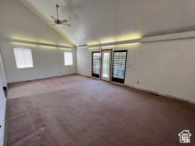 Carpeted spare room with ceiling fan and high vaulted ceiling