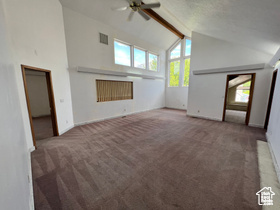 Unfurnished living room with vaulted ceiling with beams, ceiling fan, and dark carpet