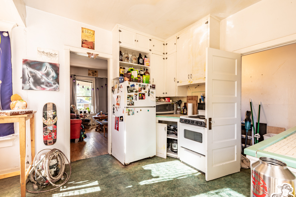 Kitchen with tile counters, white cabinetry, dark wood-type flooring, and white appliances