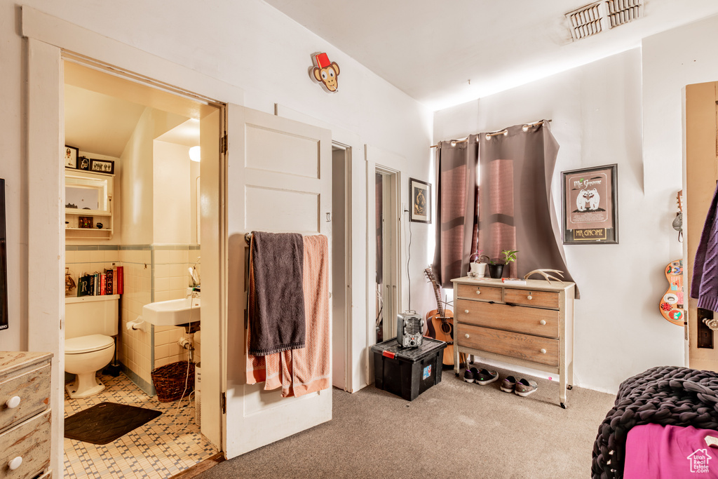 Bedroom featuring connected bathroom, tile walls, and light carpet