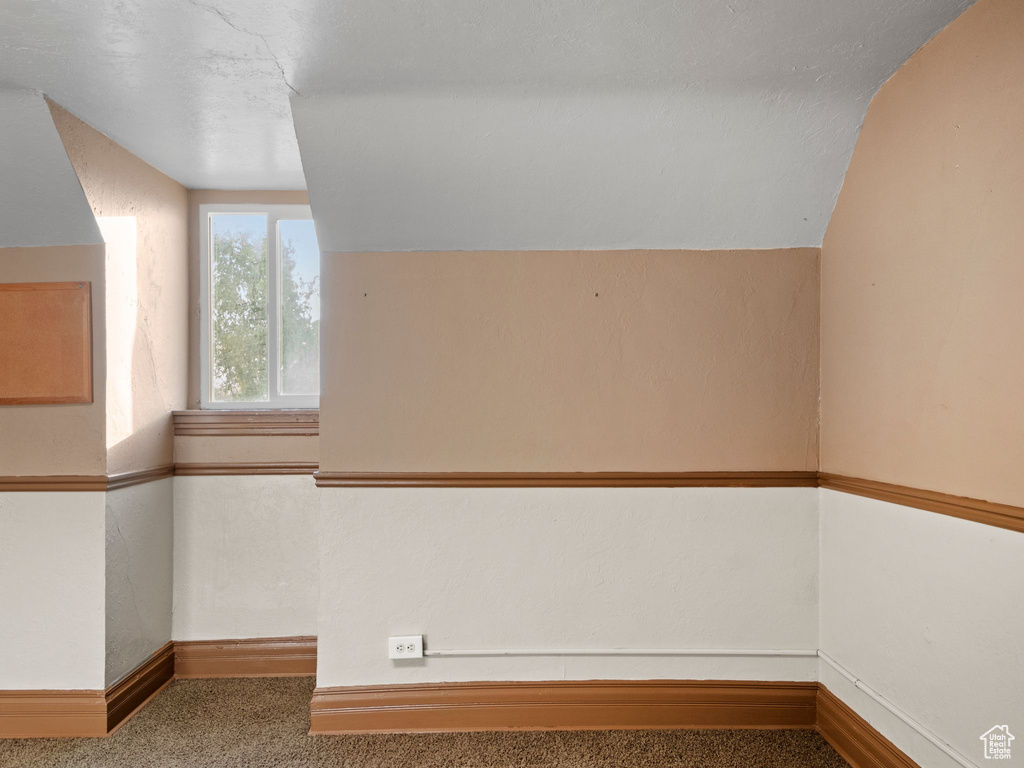 Carpeted empty room featuring a textured ceiling and vaulted ceiling